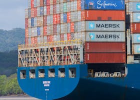 A cargo ship loaded with containers navigates the Panama Canal under clear skies.