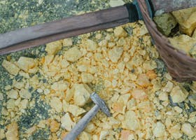 Close-up of a hammer and basket amidst yellow sulfur rocks on the ground.
